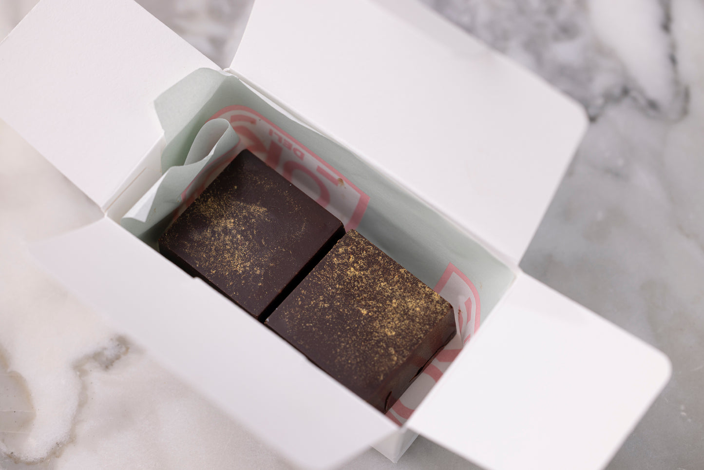 Two dark chocolate bars in a white box on a marble surface