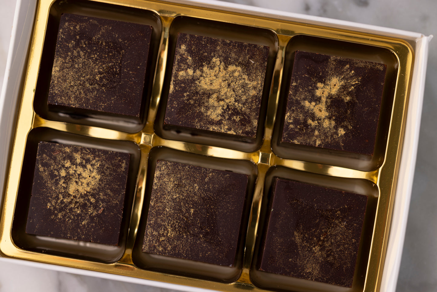 
                  
                    Box of dark chocolates with gold trim on a marble surface
                  
                