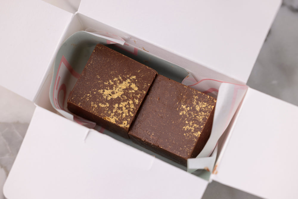 Two chocolate brownies with gold sprinkles in a white box on a gray checkered background