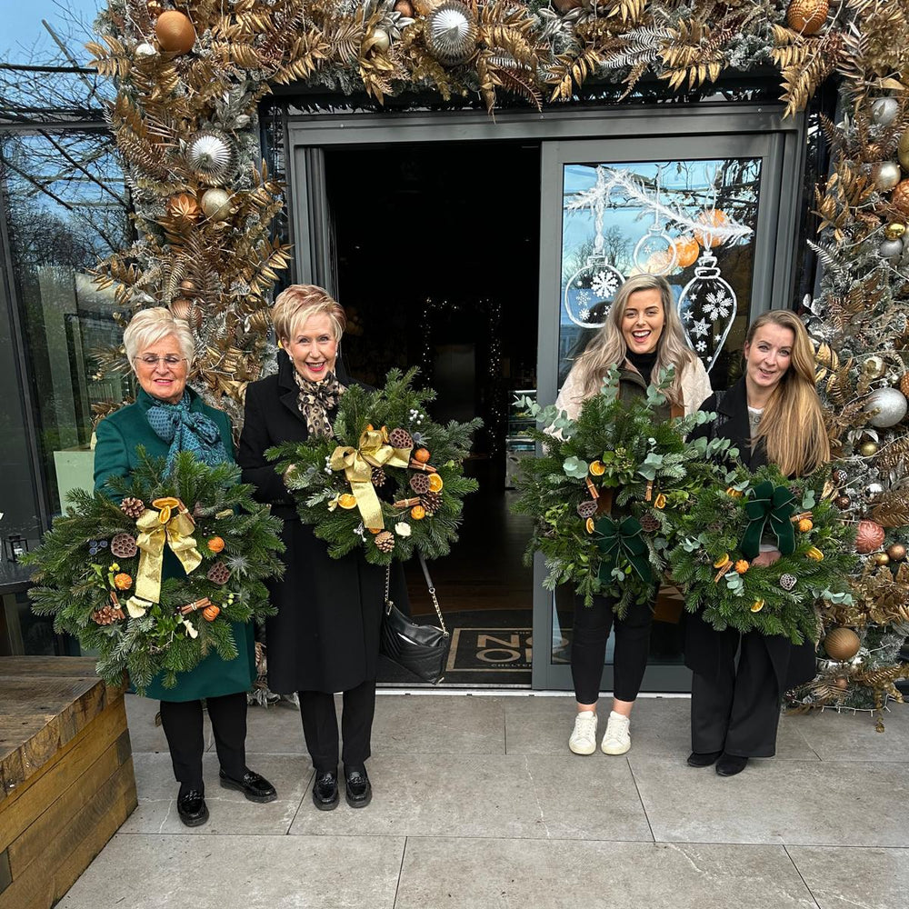 Four women holding Christmas wreaths in front of a decorated doorway.